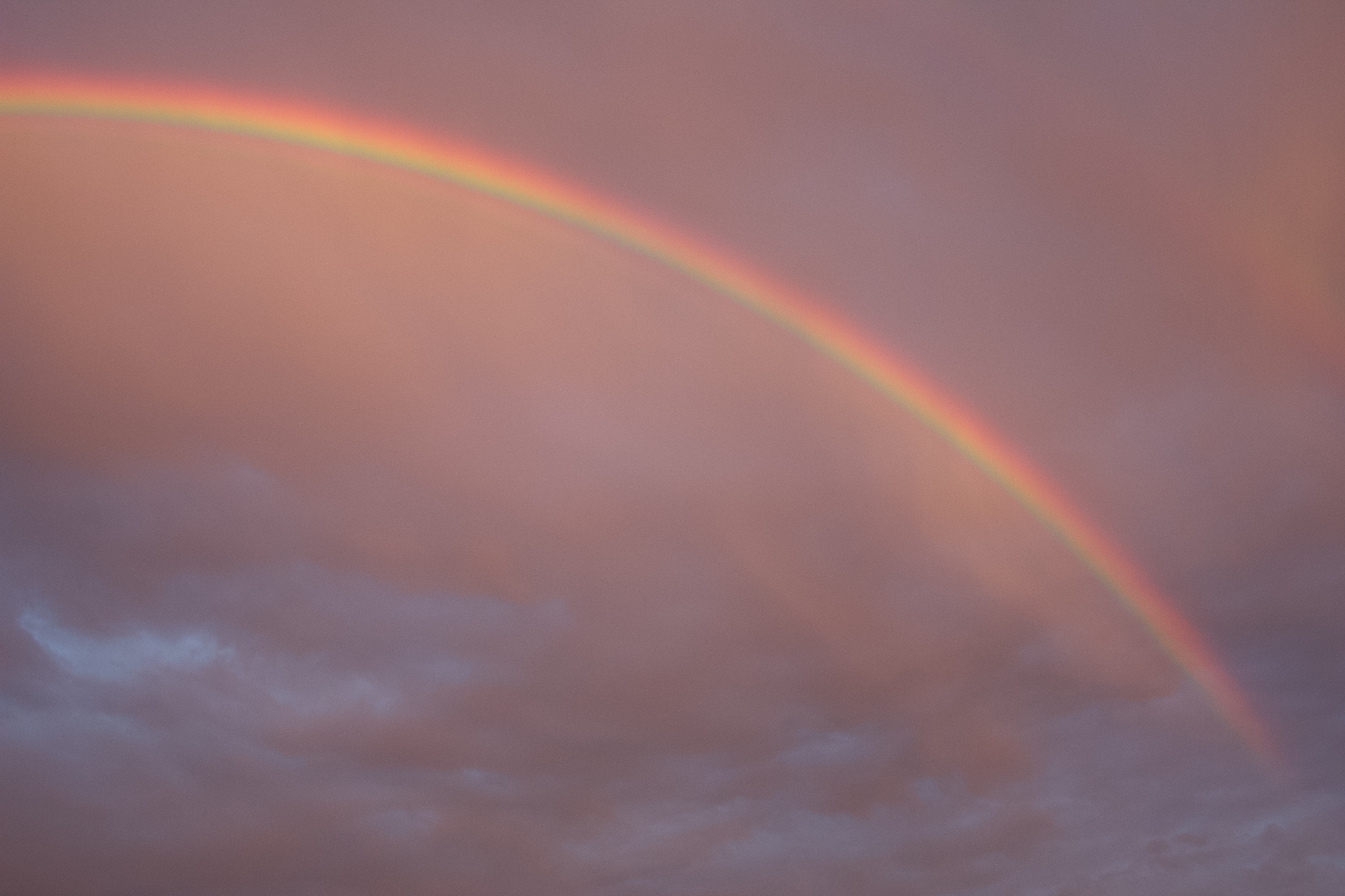 a rainbow with a background of pink and purple clouds during sunset